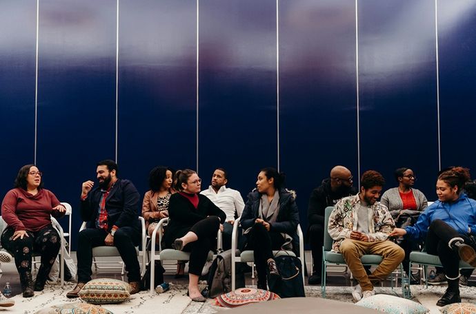 Imagen de personas reunidas en círculo sobre un césped, discutiendo ideas