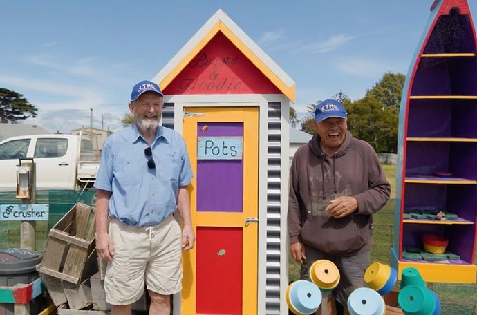 Two men standing in front of a shed that holds supplies for their community garden